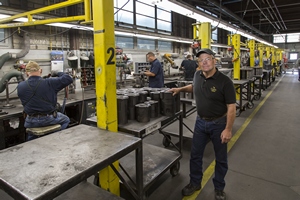 Man posing for a picture with workers working behind him.